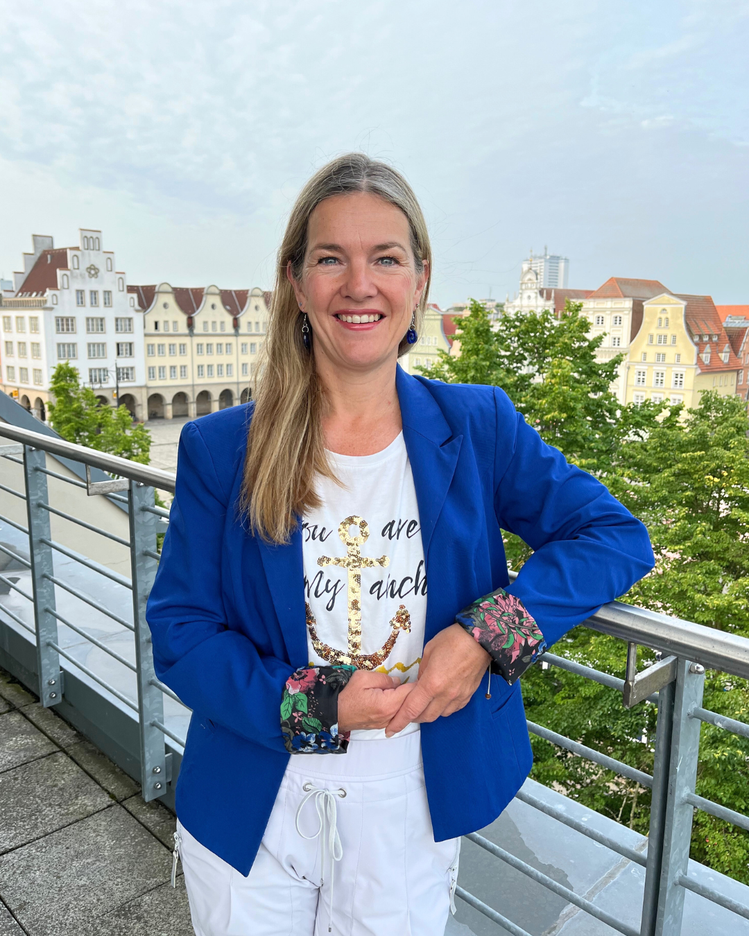 Das Bild zeigt Patricia Huber auf einem Balon mit blauem Blazer. Im Hintergrund ist der neue Markt in Rostock zu sehen.