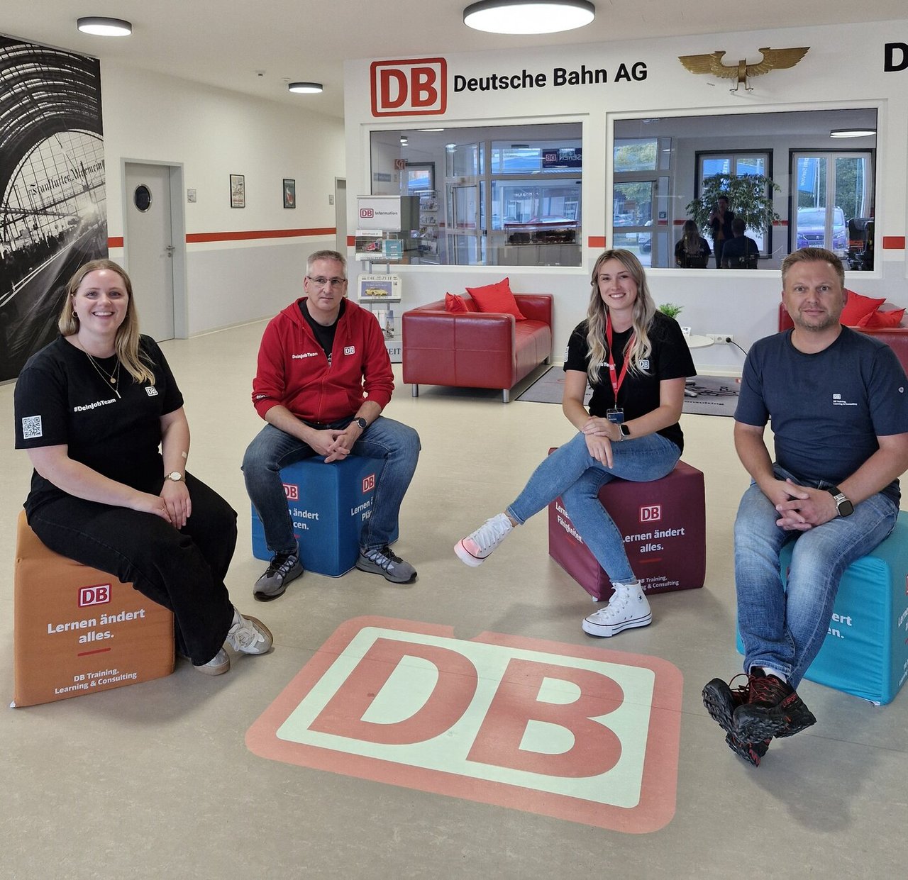 Das Bild zeigt 4 Mitarbeiter von DB auf Sitzwürfeln