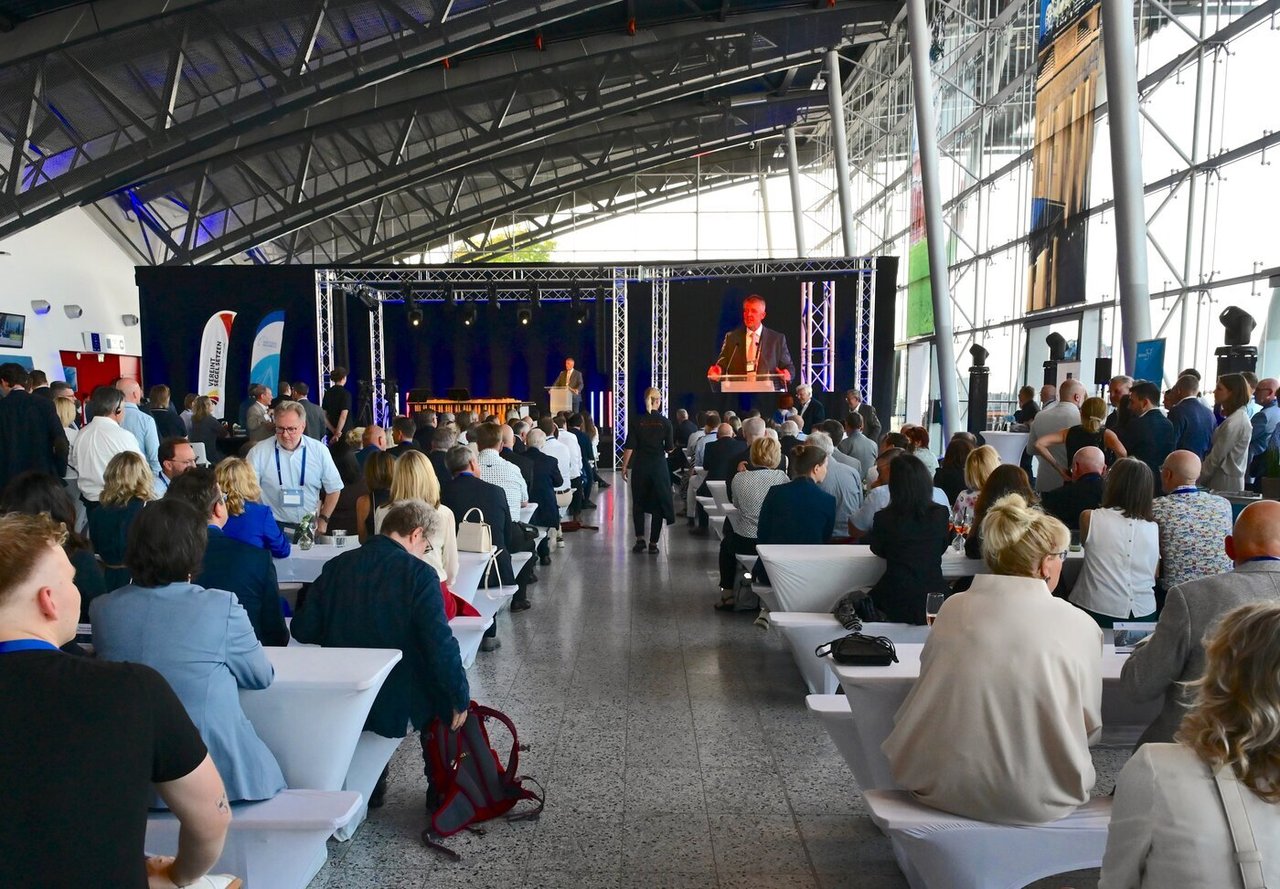 Das Foto zeigt eine Kongresshalle mit vielen Personen, welche alle einem Redner zuhören