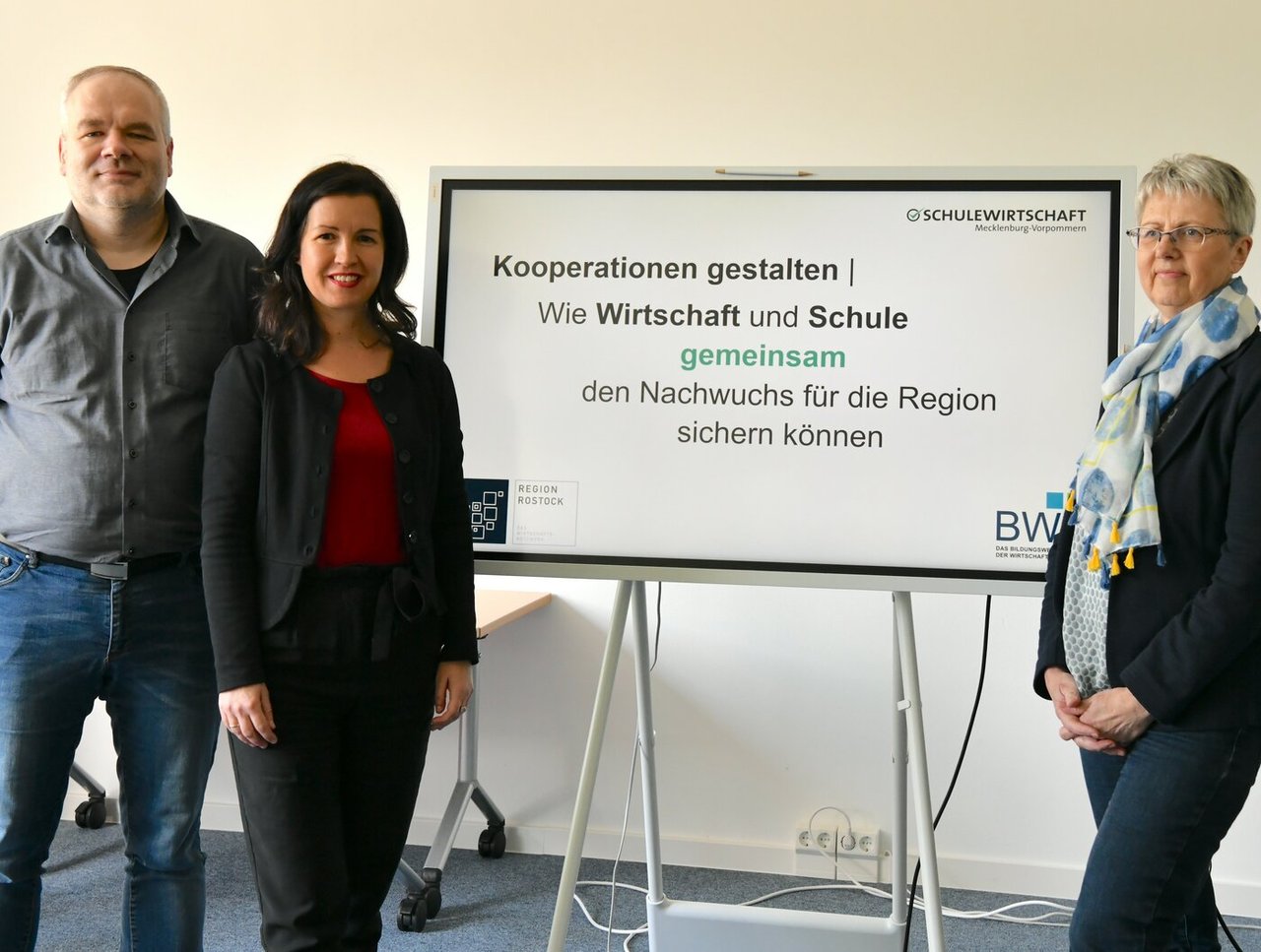 Arbeitskreis SCHULEWIRTSCHAFT Rostock zeigt ein Bild von 3 Personen vor einem Bildschirm mit einer Präsentation zum Thema "Kooperationen gestalten - Wie Wirtschaft und Schule gemeinsam für Nachwuchs die Region sichern können"